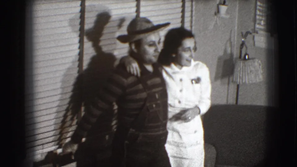 The adult couple in 1941 Joliet appears slightly turned toward the camera, standing in a private room with blinds, lamp, and chair visible.