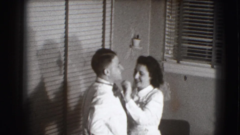 The couple face one another and laugh as the woman finishes adjusting the man's tie in the domestic Joliet setting.