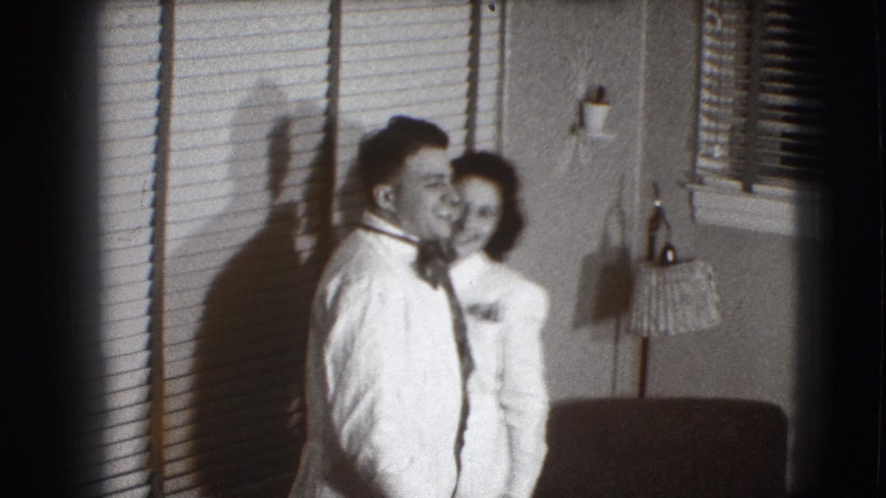 Young man and woman in light formal clothing smile beside window blinds in a room.