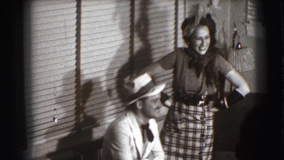 The 1941 Joliet frame shows a laughing woman standing near blinds as a seated man in a light suit and fedora turns toward her.