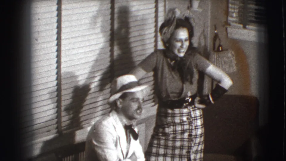 The final frame keeps the posed 1941 Joliet home setting, with the woman standing and the man seated near the chair and blinds.