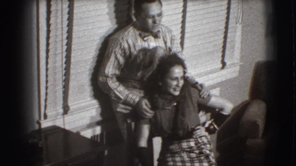 The man remains behind the seated woman in the 1941 Joliet interior, holding her shoulders as she smiles and leans forward.