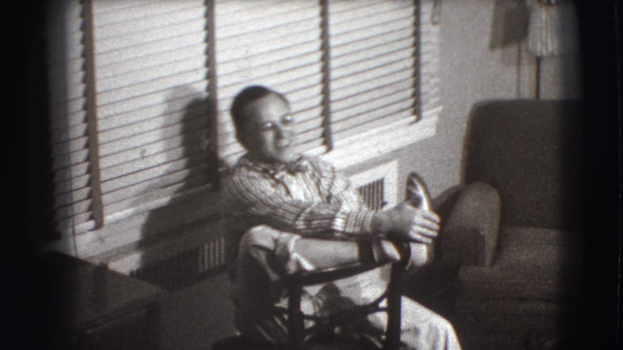 Seated man extends his hands while sitting near blinds and an armchair.