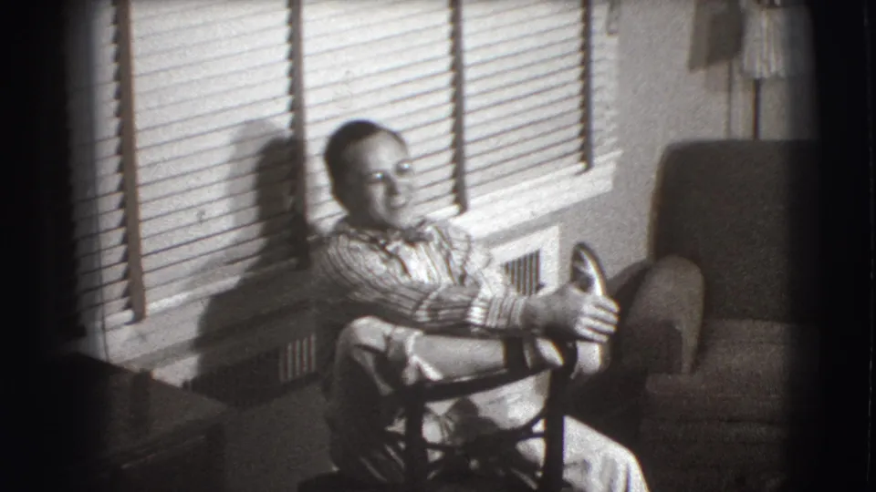 The patient sits near venetian blinds and appears to hold out his hands in the Joliet 1941 medical-room footage.
