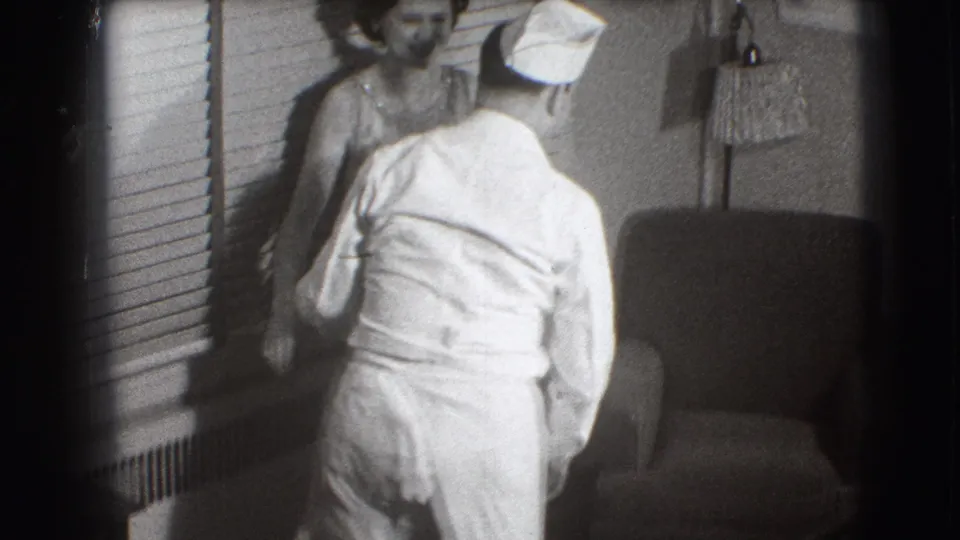 A nurse in a white uniform and cap approaches the seated patient in the 1941 Joliet medical-care home movie.