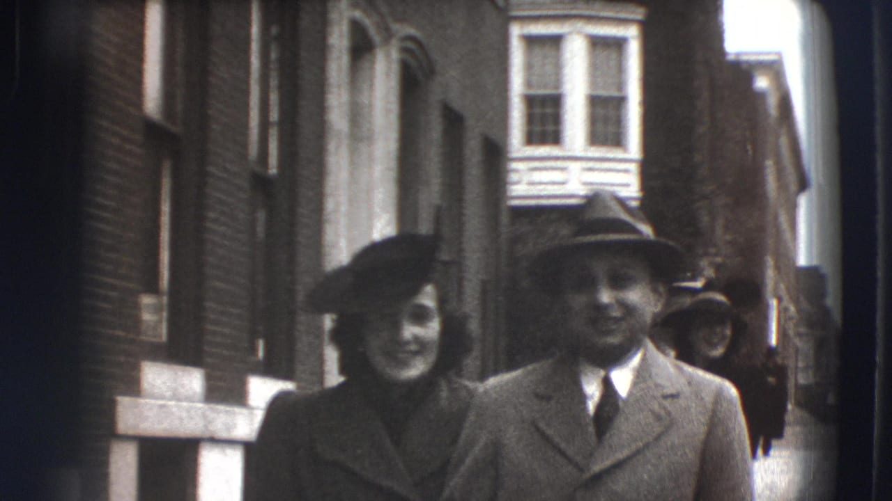 Well-dressed couple walking toward the camera on a narrow city street.