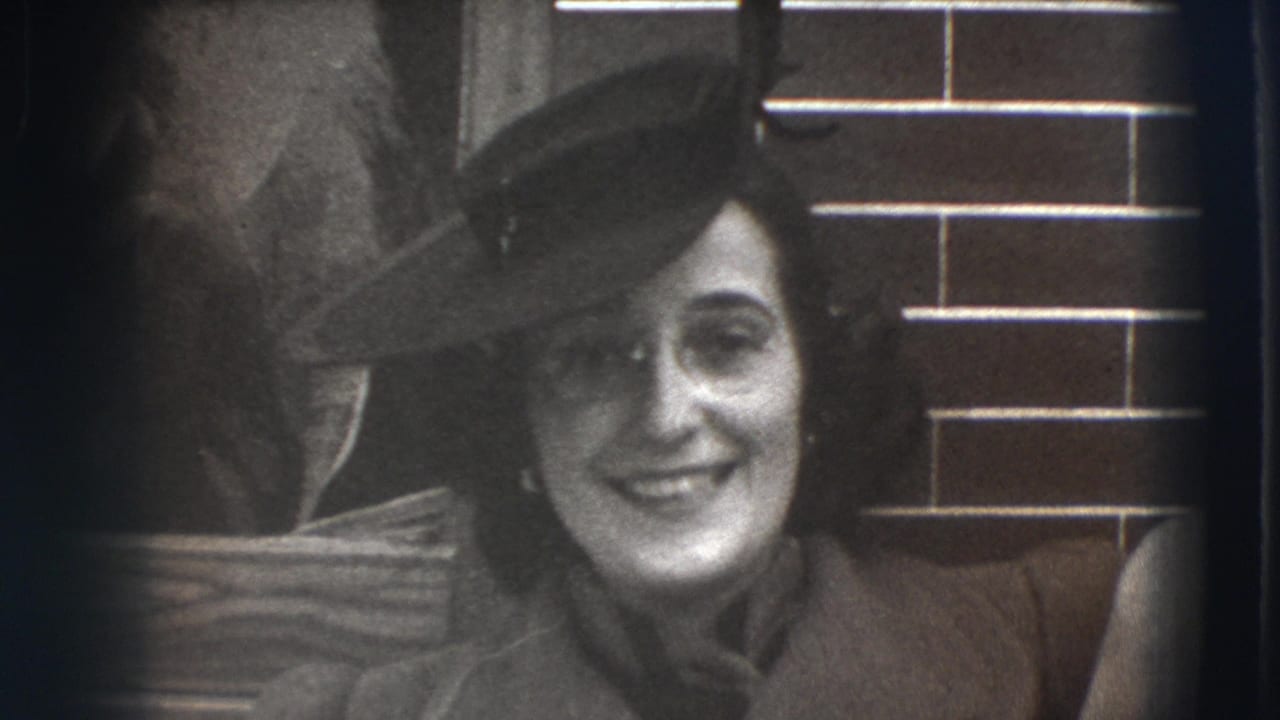 Woman in a dark hat and coat smiles near a brick wall and doorway.