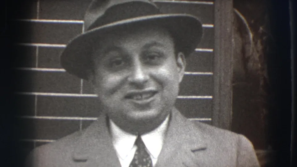 A man in a fedora, suit, and tie smiles toward the camera in 1941 Joliet, Illinois home-movie footage.