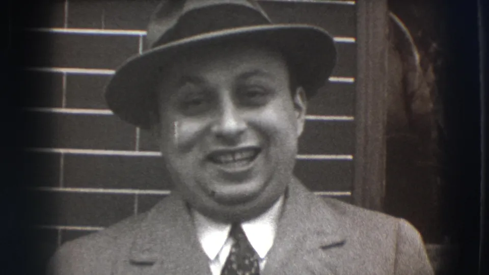 Closer 8mm view of the smiling man in a fedora and suit, framed against brickwork in Joliet, Illinois.