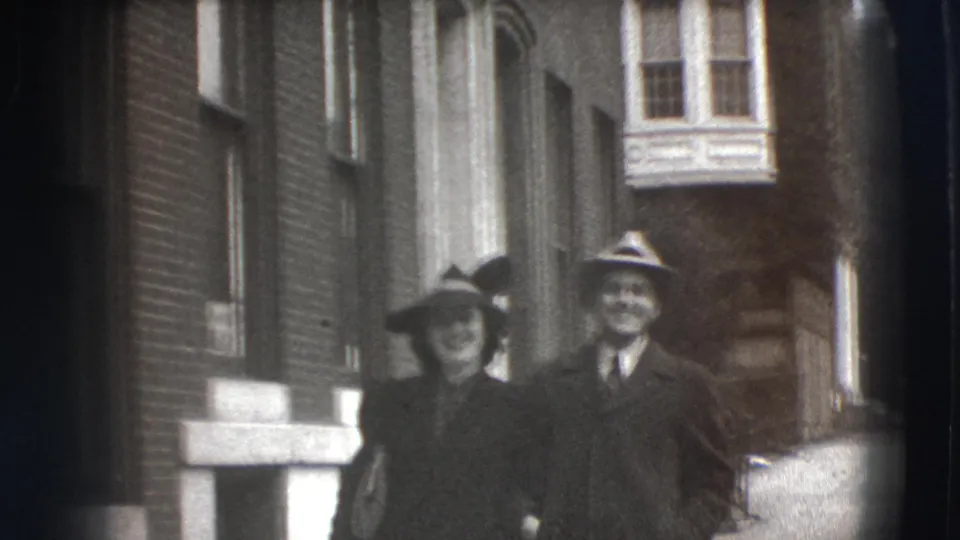 The woman and man walk together along a Joliet city sidewalk, with brick buildings and windows behind them.
