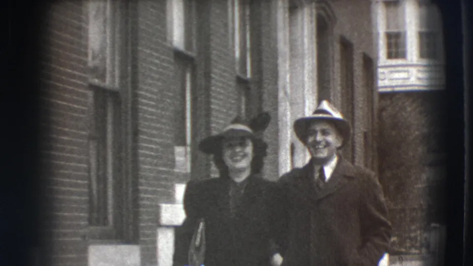 In 1941 Joliet, Illinois, a well-dressed couple smiles near a brick building facade in grainy 8mm home-movie footage.