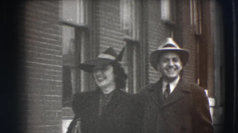 The woman and man remain close together on a Joliet street, smiling beside brick architecture in a 1941 8mm frame.