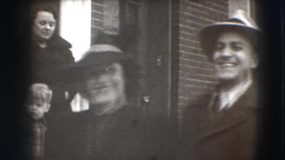 A soft 8mm frame shows the smiling couple close to the camera, with additional figures partly visible at the left edge.