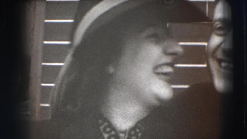 A woman in a wide-brimmed hat laughs beside a man, with brickwork behind them in the supplied Joliet street footage.