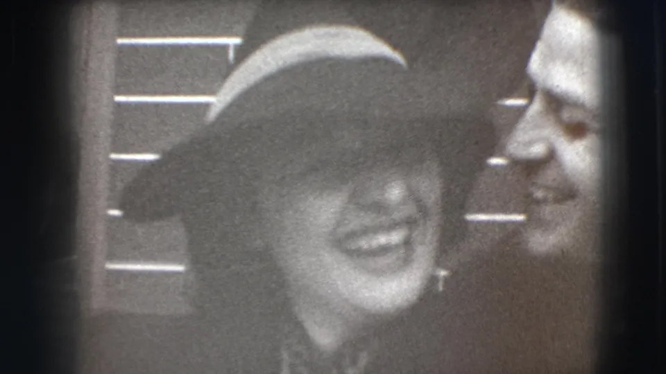 The woman in a broad hat laughs between two men, one close beside her, in this 1941 Joliet home-movie frame.