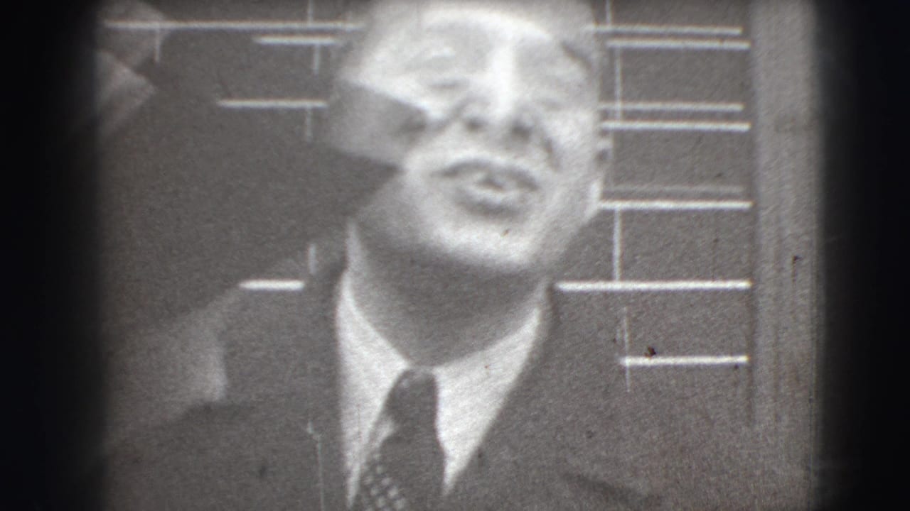 Close-up of a suited man in front of horizontal wall lines.