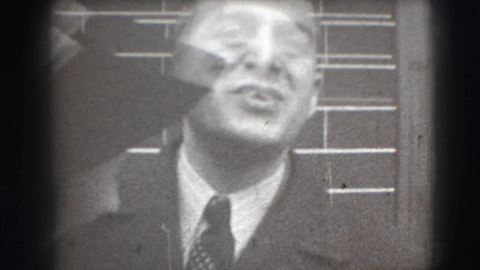 Black-and-white 1941 Joliet home-movie frame showing a suited man close to camera before meeting-hall views.