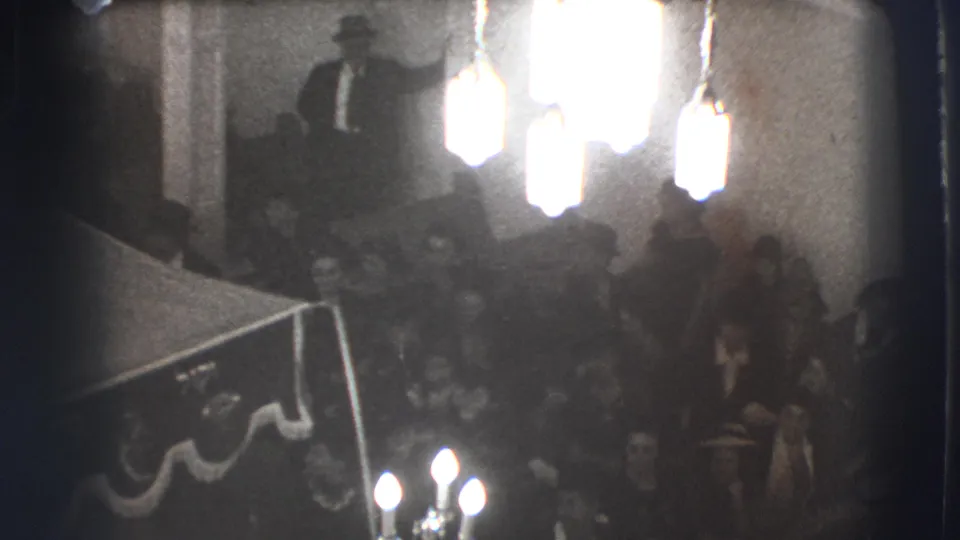 Elevated black-and-white view of a crowded Joliet meeting room with men seated below bright fixtures.