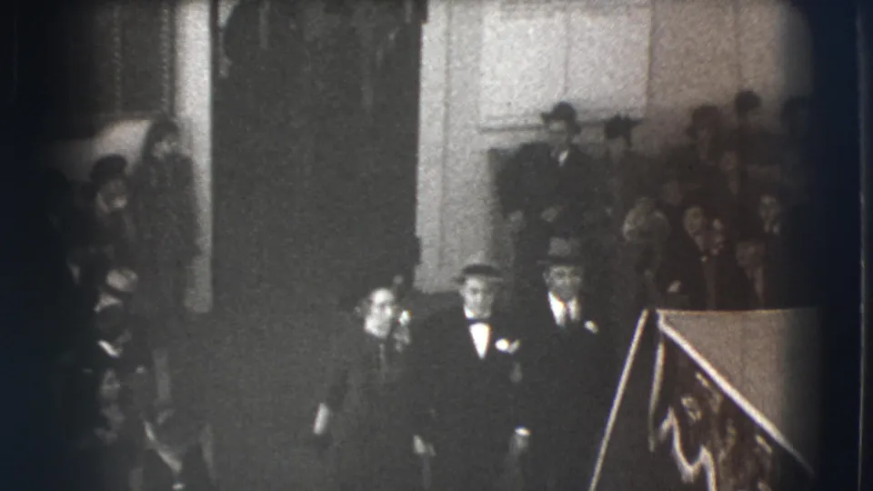 A 1941 Joliet frame shows a woman and two men in formal dress moving through an indoor crowd, with hats and suits visible around them.