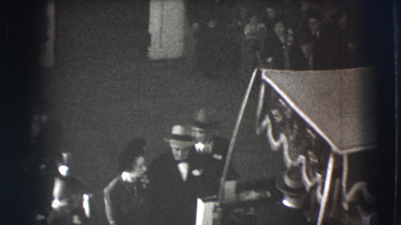 Elevated view of suited men near a decorated stair or podium inside a dim hall.