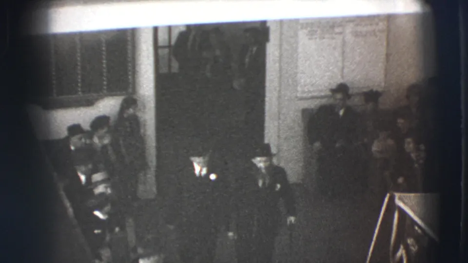 1941 Joliet frame with two suited men in the foreground and other guests seated or standing along an interior wall.