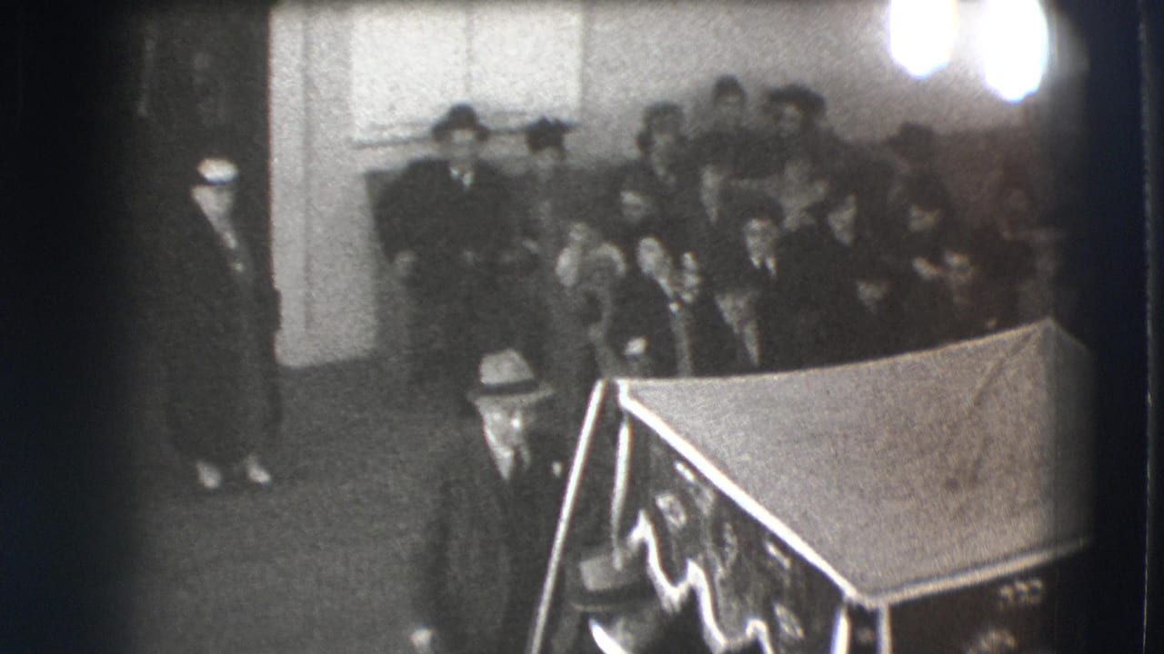 Mourners gather near a draped casket in a dim black-and-white interior.
