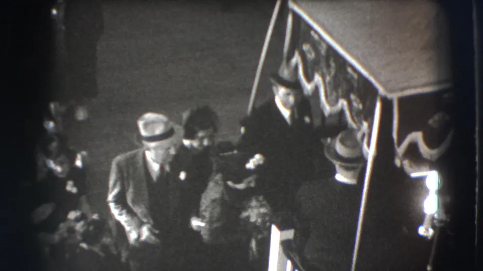 The 1941 Joliet home movie shows mourners walking or pausing beside the casket during an indoor funeral procession.