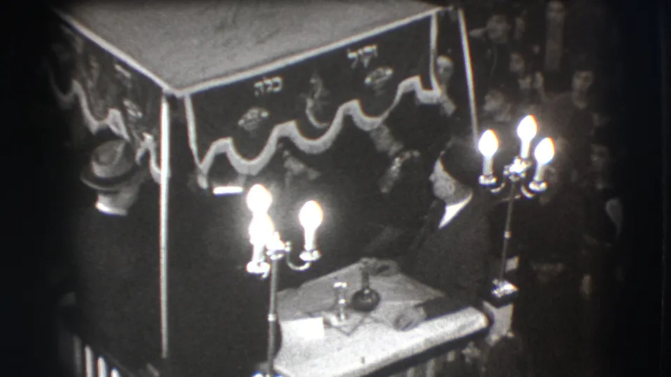 1941 Joliet home-movie frame showing suited men beneath a decorated canopy, with candelabras and a table before a close audience.
