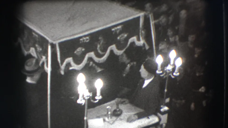 Final 1941 Joliet frame with a suited man near the decorated canopy, bright candelabras, table objects, and spectators at the edge.