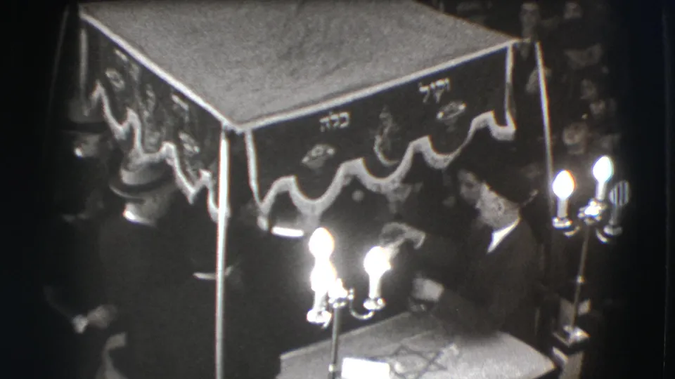 Candlelit 1941 Joliet ceremony scene with a seated man under a Hebrew-inscribed canopy and other figures nearby.