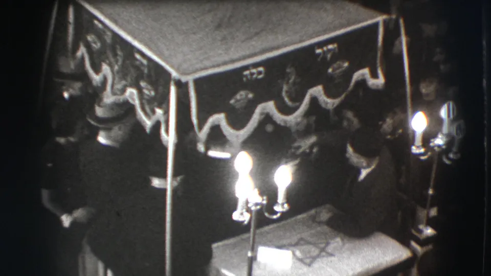 End frame from 1941 Joliet footage showing men in formal attire around a candlelit table and decorated Hebrew canopy.