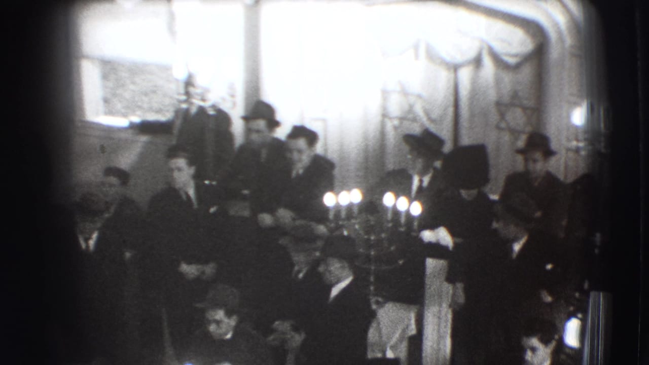 Men in suits gather indoors near lit candles and Star of David decorations.