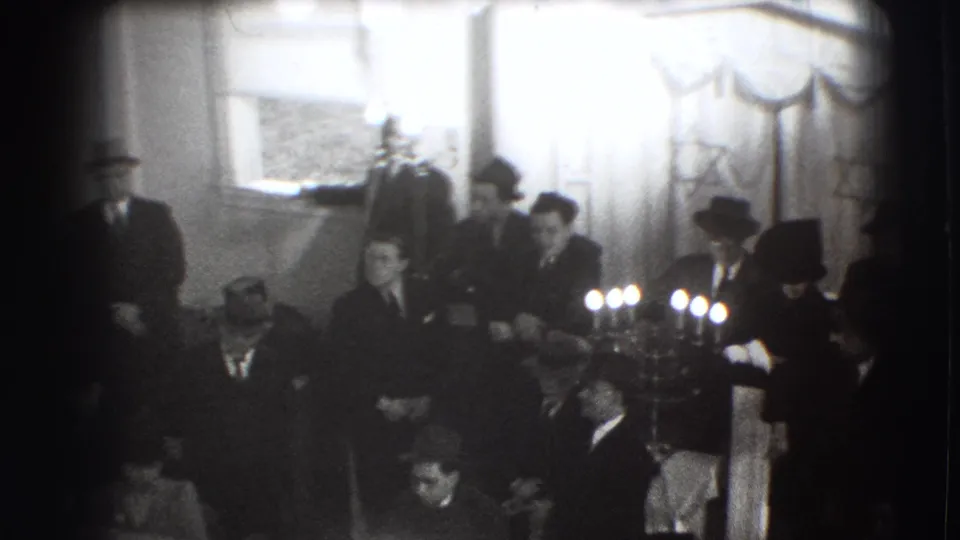 Formal-dressed men in a Joliet interior stand and sit beside bright ceremonial candles and Jewish decorations in 1941 footage.