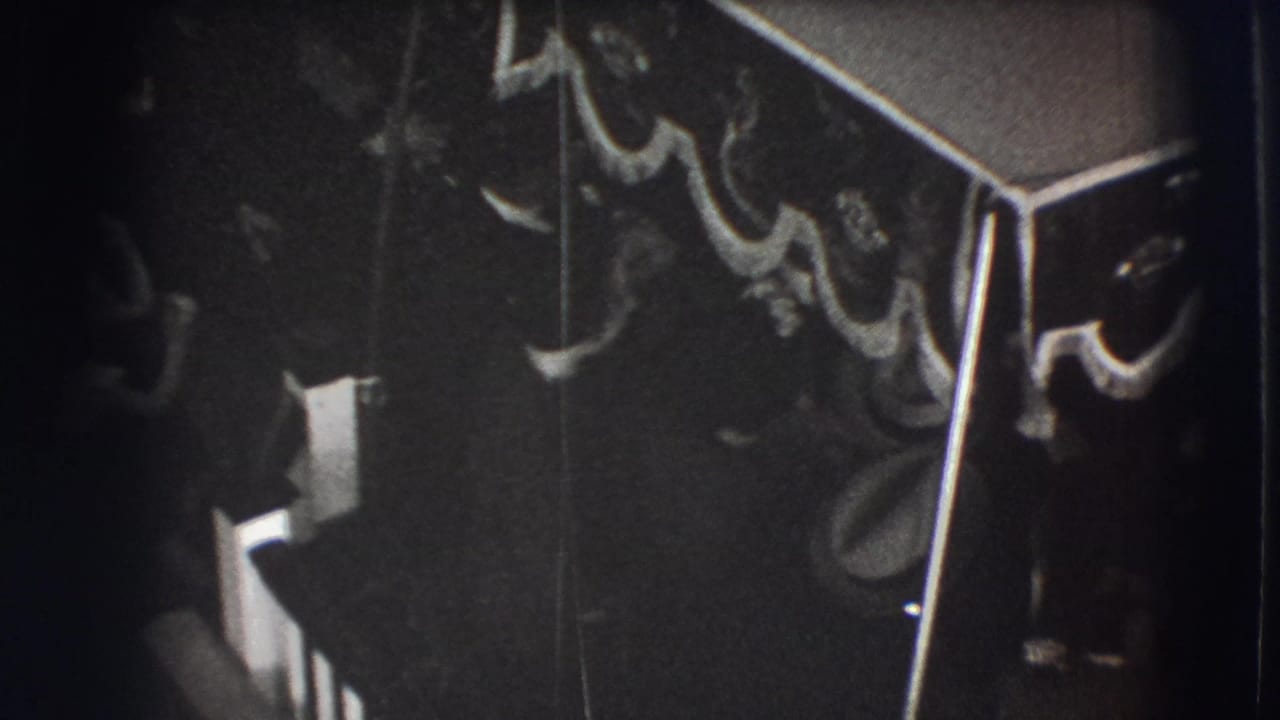 Backlit 1941 Joliet home-movie frame showing a dim formal interior, tasselled canopy, and silhouetted guests.