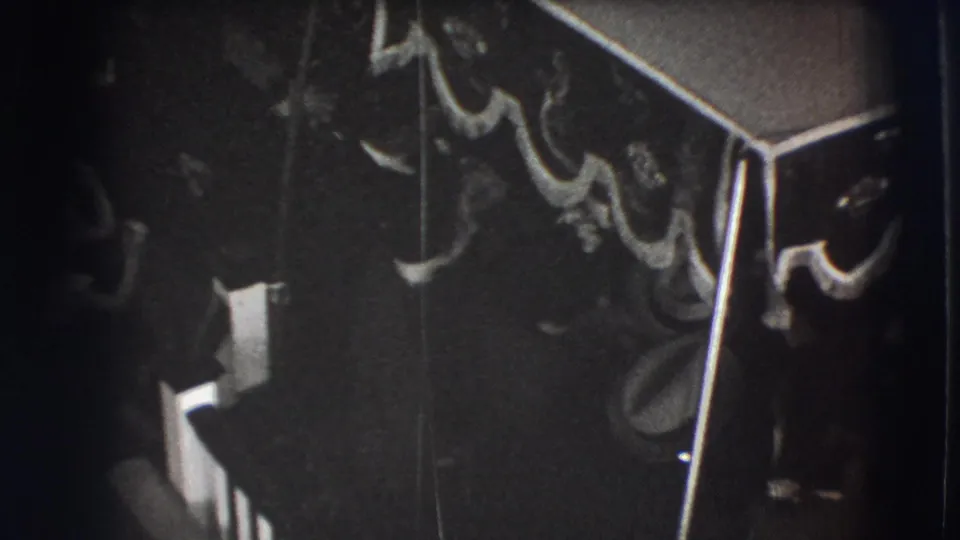 Backlit 1941 Joliet home-movie frame showing a dim formal interior, tasselled canopy, and silhouetted guests.