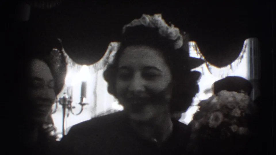A woman in formal dress and a flower-trimmed hat smiles toward the camera during the Joliet, Illinois home-movie gathering.