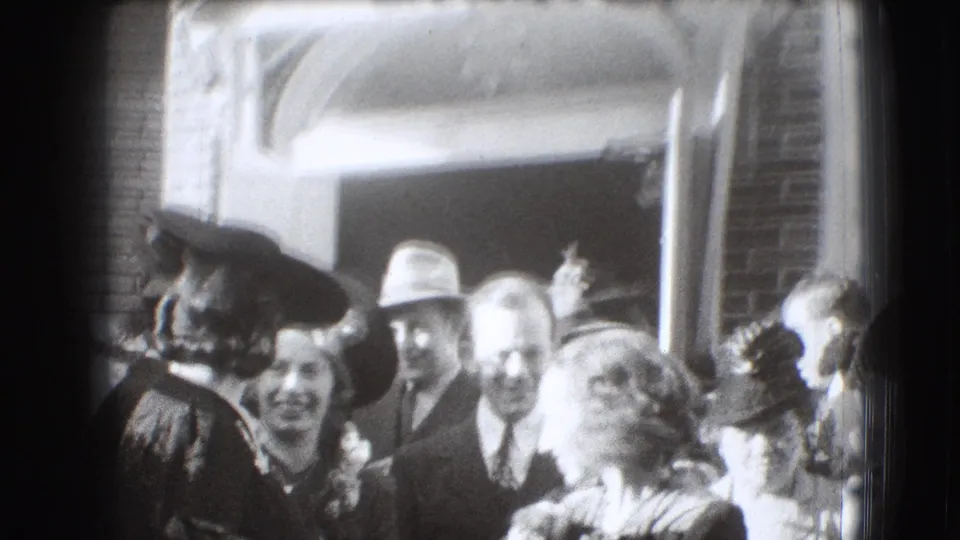 1941 Joliet home-movie frame showing adults in period hats and suits clustered near a brick building doorway.