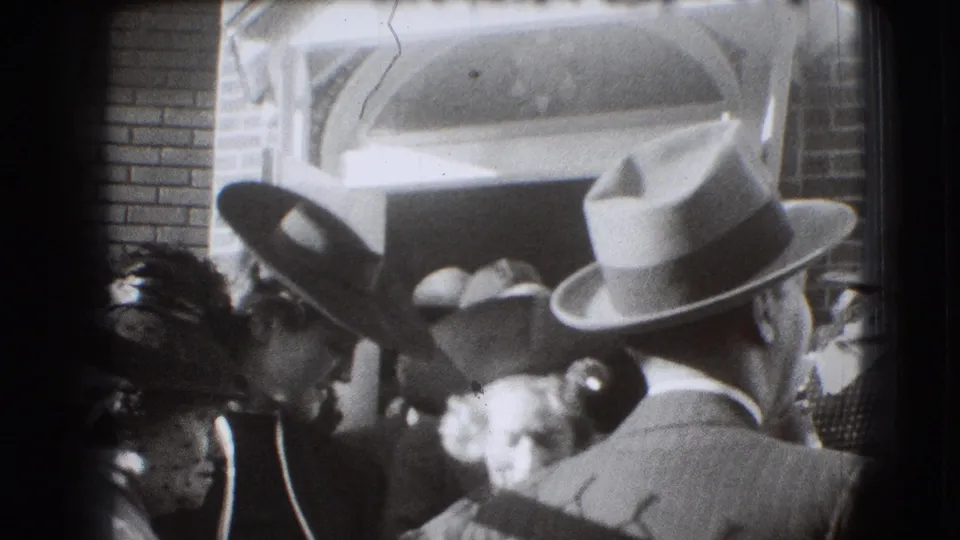 1941 Joliet frame showing a man in a light fedora from behind amid a dense crowd outside the brick entrance.