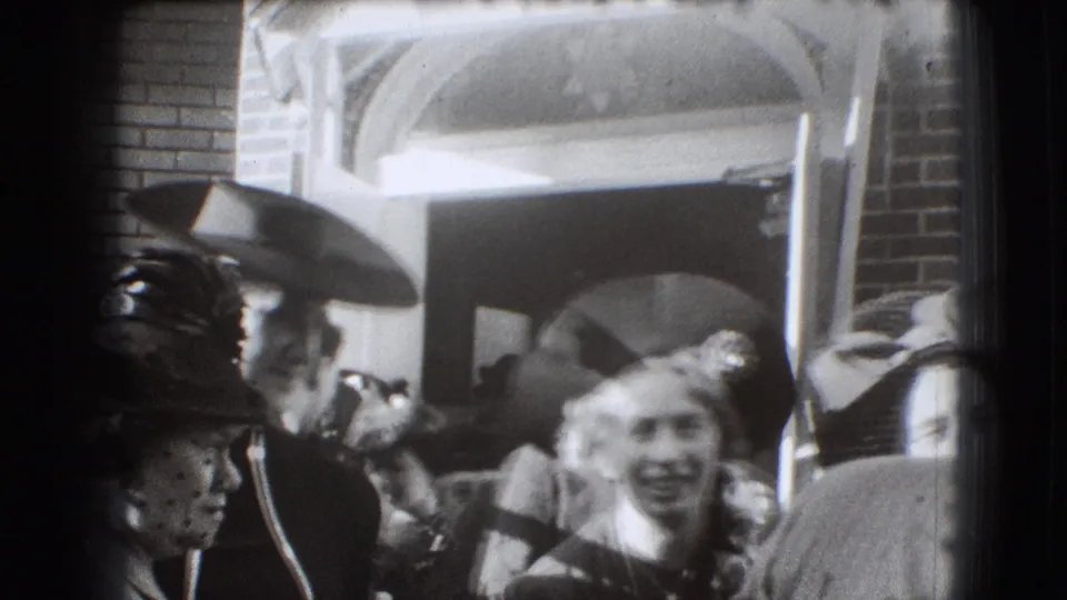 1941 Joliet home-movie frame showing men and women in hats near a brick building entrance, with a smiling woman close to the camera.