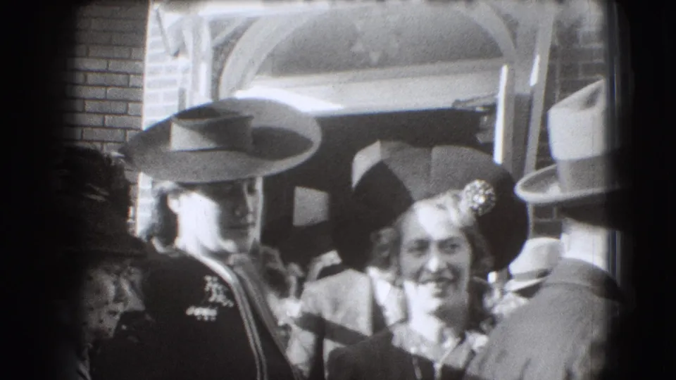 1941 Joliet frame with a smiling woman in the foreground and adults in wide-brimmed hats clustered outside a brick entrance.