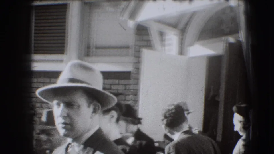 1941 Joliet home-movie frame showing a man in a light hat in the foreground as other adults move near an open doorway.