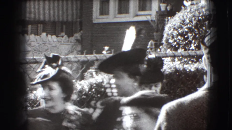 1941 Joliet home-movie frame with women in brimmed hats moving through a crowded outdoor residential gathering.