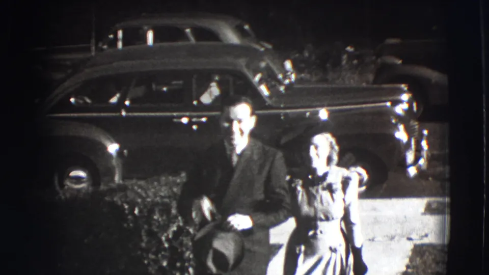 The couple comes closer to the camera in Joliet, Illinois, with the woman's hat and a rounded 1940s automobile visible behind them.