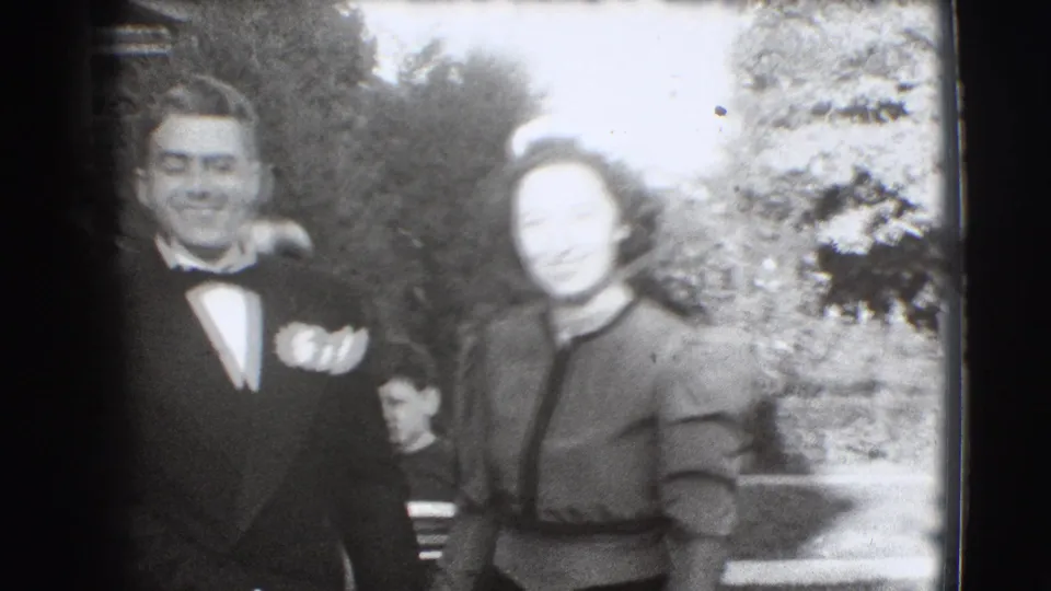 In Joliet, Illinois, 1941 footage, a tuxedoed young man and formally dressed woman pose together outdoors near a porch and garden.
