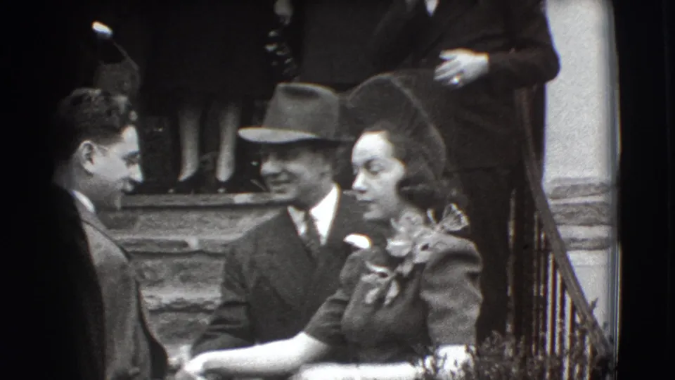 Formal guests in 1941 Joliet footage gather on steps, with men in suits and hats and a woman wearing a corsage.