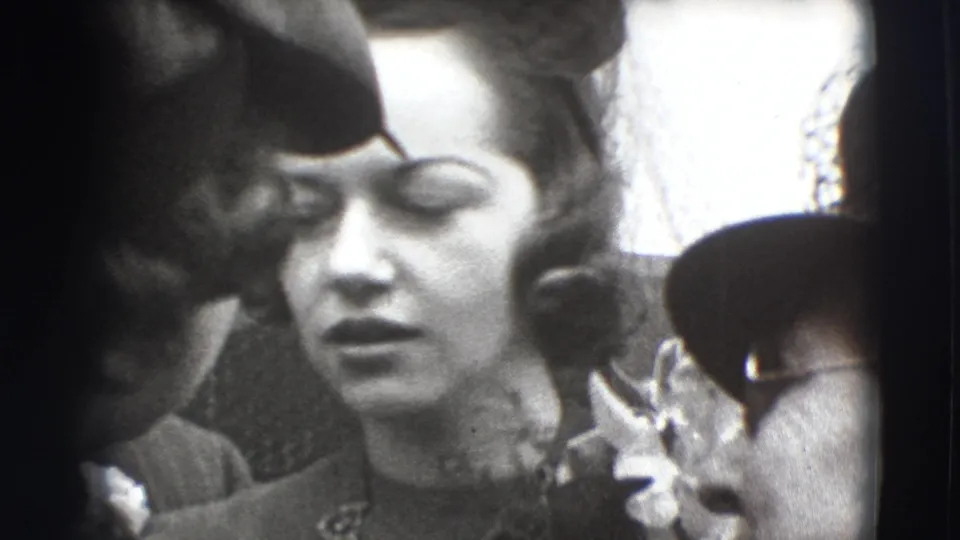 Close-up from the 1941 Joliet home movie shows a woman in formal dress and hat surrounded by other adults in hats.