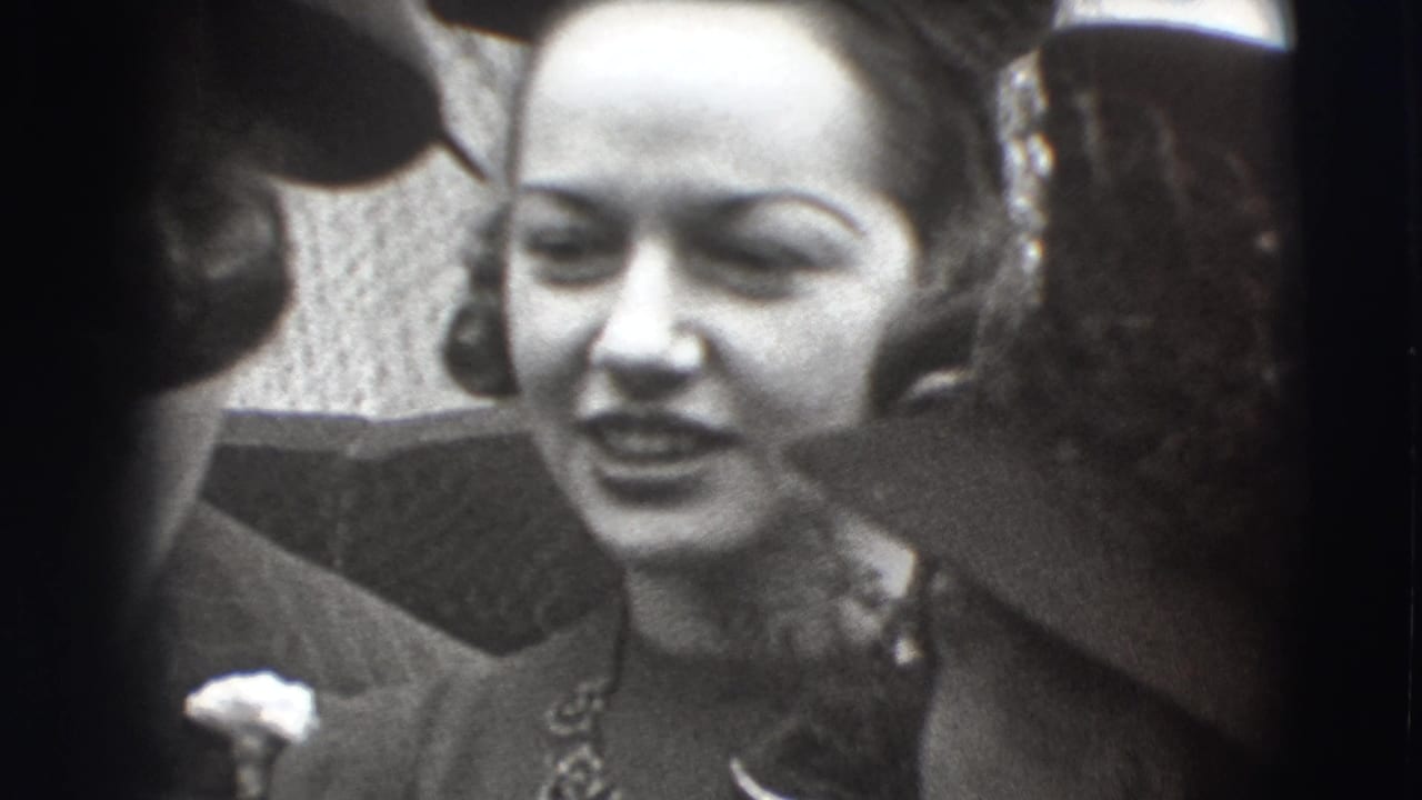 In Joliet, Illinois home-movie footage from 1941, a woman in formal dress and a decorative hat stands close to other adults.