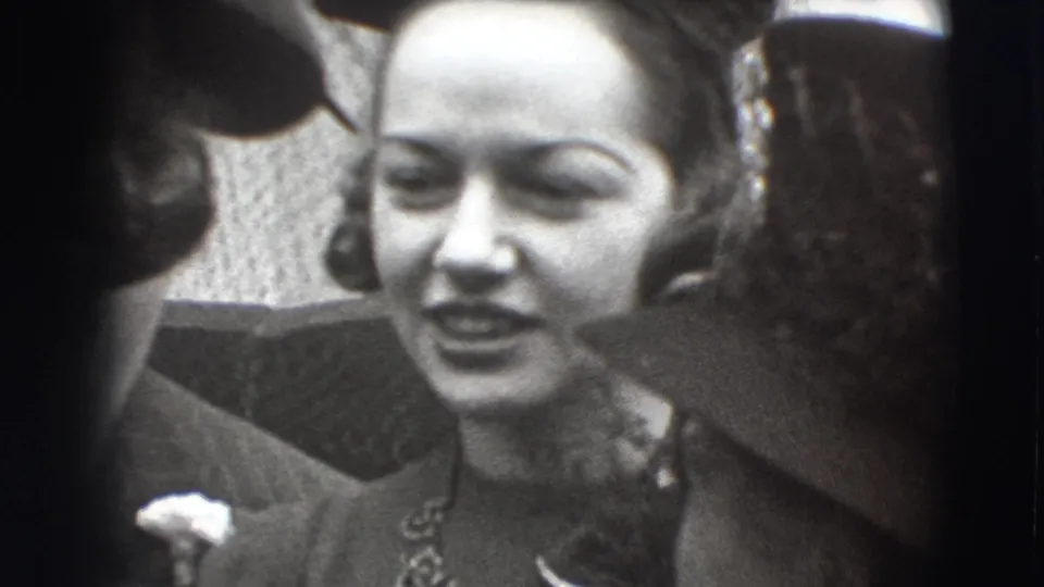 In Joliet, Illinois home-movie footage from 1941, a woman in formal dress and a decorative hat stands close to other adults.