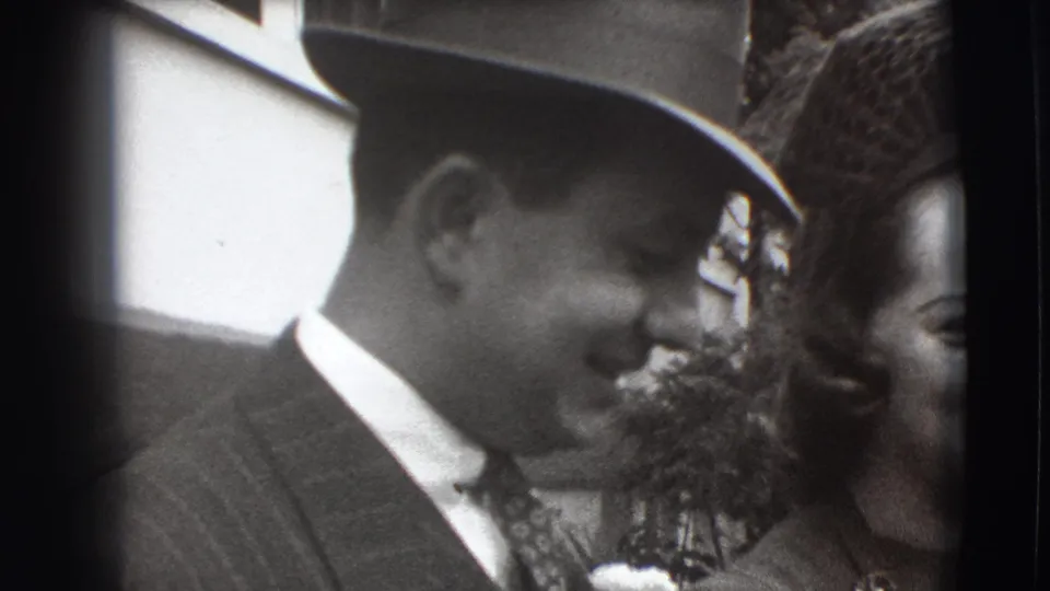 A man in a fedora and pinstripe suit smiles beside a woman in 1941 Joliet home-movie footage.
