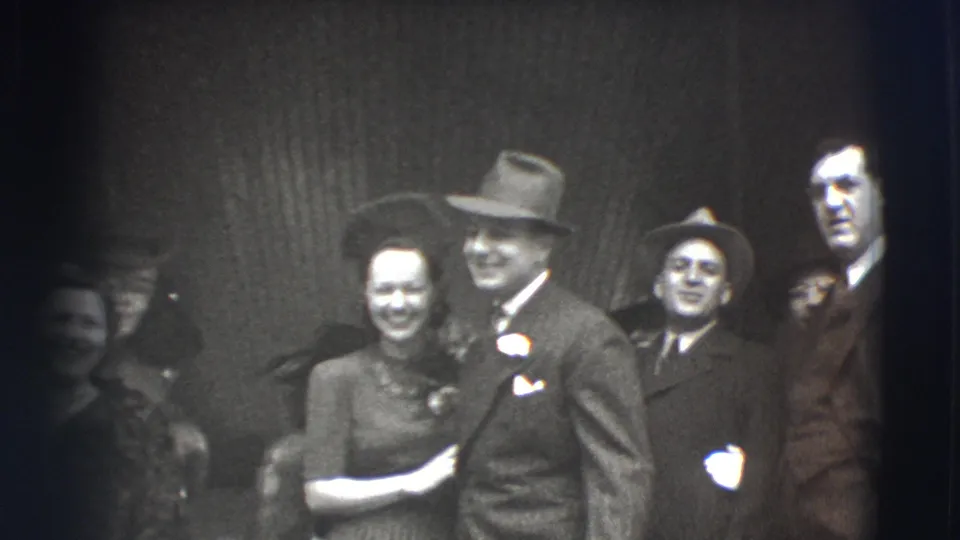 In Joliet, Illinois, a smiling woman stands close to a suited man in a fedora while other formally dressed adults look on.